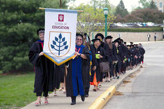 Graduates march down a sidewalk holding a School of Education banner.